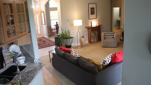 Una sala de estar con un sofá gris, una mesa de centro y una chimenea. Hay un comedor con un aparador de madera y una araña.