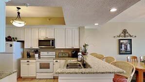 A kitchen with white cabinets, a microwave, an oven, a sink, and a dining area with wicker chairs.