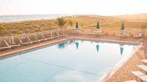 A swimming pool with lounge chairs and a view of the beach.
