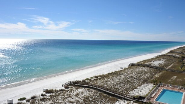 A beach resort with a clear view of the ocean, a sandy beach, and a pool area.