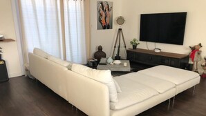 Un soggiorno moderno con un divano, un tavolino, un treppiede e una TV a schermo piatto.
