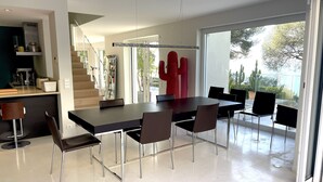 Un espace repas moderne avec une grande table et des chaises, un coin cuisine équipé d’appareils électroménagers et un escalier menant à un autre niveau.