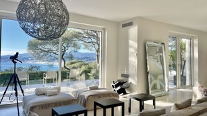 Un salon moderne doté d’une grande fenêtre donnant sur un paysage magnifique, d’un luminaire suspendu et d’un trépied avec un appareil photo.