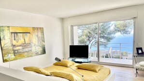 Une chambre moderne dotée d’un grand lit, d’un téléviseur à écran plat et d’un balcon offrant une vue sur la mer.