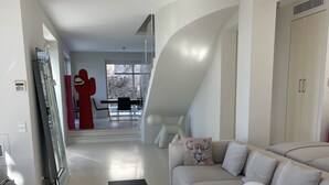 Un salon moderne avec un canapé, deux tables d’appoint noires, une sculpture rouge et, au fond, un coin repas.