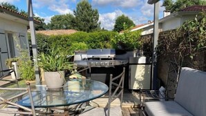 A patio with a glass table, metal chairs, a barbecue grill, and a white sofa. - Villa des Doudoux (Andernos-les-Bains)
