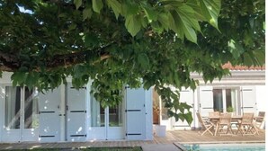 A poolside area with a wooden deck, a pool, and a covered seating area with chairs. - Villa des Doudoux (Andernos-les-Bains)