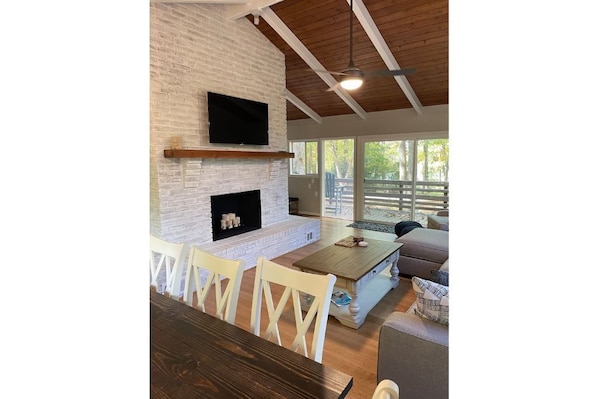 A living room with a fireplace, a television mounted on the wall, and a large window offering a view of the outdoors.