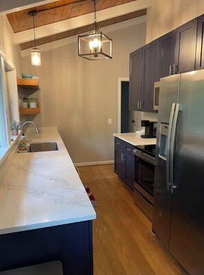 A modern kitchen with dark cabinets, a stainless steel refrigerator, and a marble countertop.