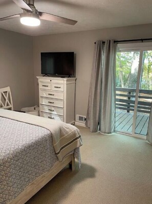 A bedroom with a bed, a TV on a dresser, and a balcony with curtains.