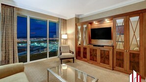 Amplia sala de estar con televisor grande, asientos cómodos y vistas a un paisaje urbano al atardecer.