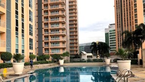Une piscine entourée de grands immeubles dotés de balcons, de plantes en pot et surplombant un ciel dégagé.