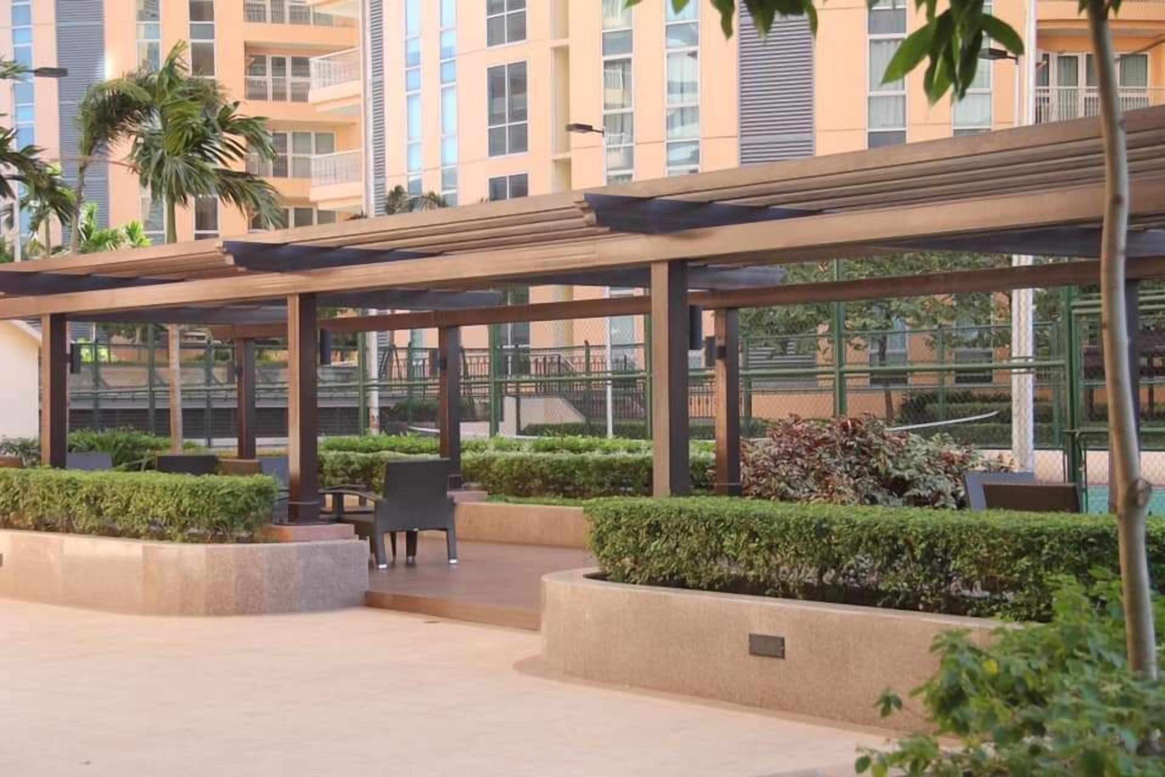 A covered outdoor area with seating and planters, surrounded by buildings.