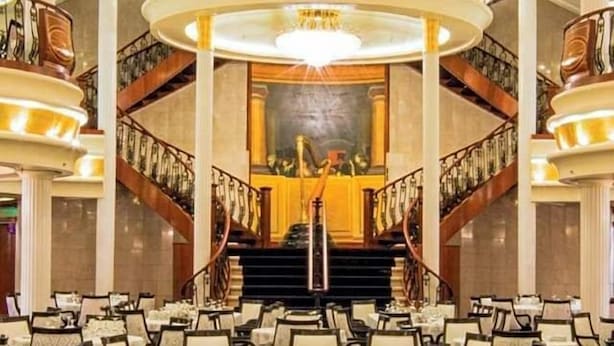 Un vaste salon de bal orné d’un grand lustre, doté de plusieurs niveaux de balcons et d’un escalier central.