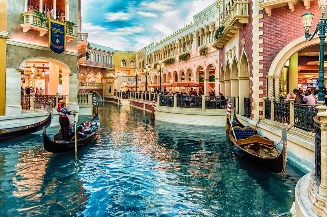 A canal with gondolas, historic buildings, and outdoor seating areas.