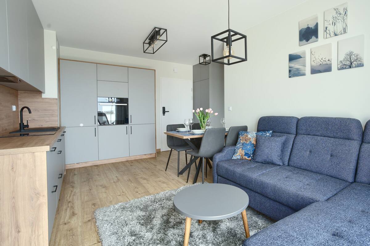 Una sala moderna con un sofá azul, una mesita redonda y un comedor con mesa y sillas.