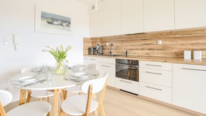 Une cuisine moderne avec des meubles blancs, un plan de travail en bois et un coin repas comprenant une table en verre et des chaises blanches.