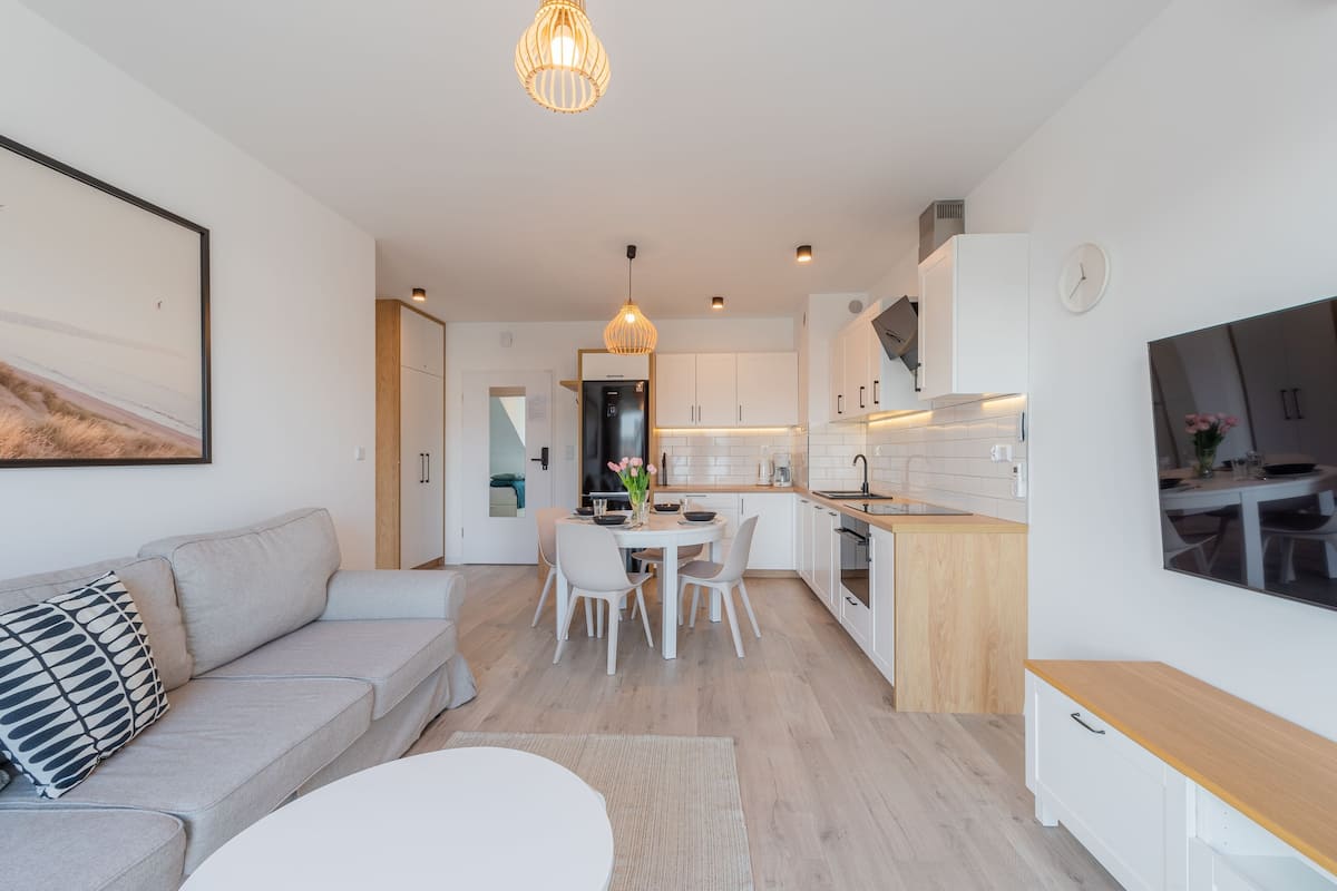 Una cocina moderna con armarios blancos, un comedor con una mesa redonda y sillas, y una sala de estar con un sofá y una televisión.