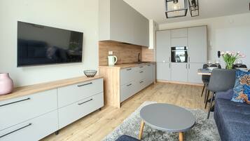 A modern kitchen with a flat-screen TV, wooden countertop, and grey cabinets.