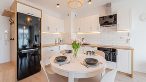 A modern kitchen with white cabinetry, a black refrigerator, a round dining table with chairs, and a pendant light.