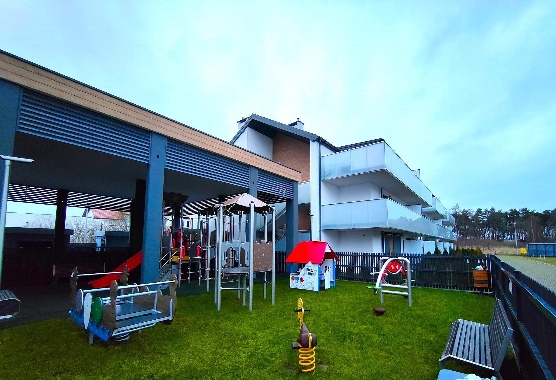 Un edificio moderno con un área exterior cubierta que incluye juegos infantiles y una pequeña estructura tipo casa.