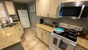 A kitchen with granite countertops, white cabinets, a stainless steel microwave, a stove with pots, and a refrigerator.