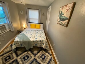A bedroom with a bed, a nightstand, a lamp, a window with curtains, and a wall with a painting.