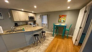 A compact kitchen with a central island, a dining area with a table and chairs, and a small window with blinds.
