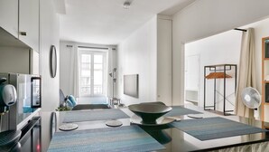A modern kitchen with a central island, a dining area with a large table, and a view of the city through a window. - Nice Apartment at 10 min From Bastille (Paris)