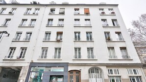 A multi-story building with a row of balconies, a ground-level entrance with a glass facade, and a large arched door. - Nice Apartment at 10 min From Bastille (Paris)