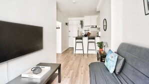 A modern living room with a flat-screen TV, a grey sofa, and a small table with a book and a decorative item. - Nice Apartment at 10 min From Bastille (Paris)