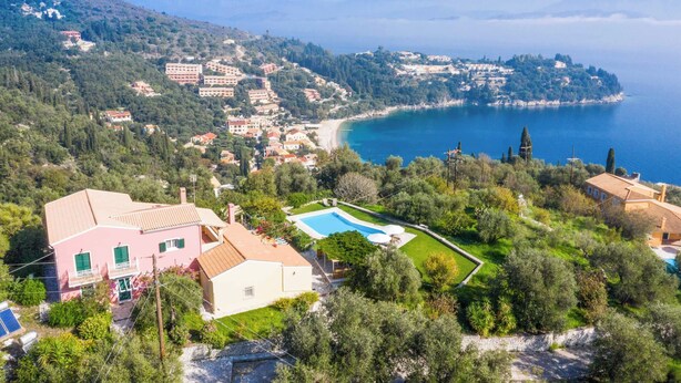 Una villa costera con piscina, rodeada de vegetación exuberante y con vistas a una bahía.