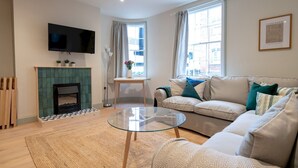 Una sala de estar moderna con chimenea, un sofá, una mesa de centro de vidrio y un televisor montado en la pared.