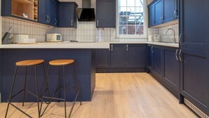 Una cocina moderna con armarios azul oscuro, una encimera blanca, dos taburetes de madera y un ventanal grande.