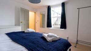 Un dormitorio con cama, ventana con cortinas, radiador y puerta que da a otra habitación.