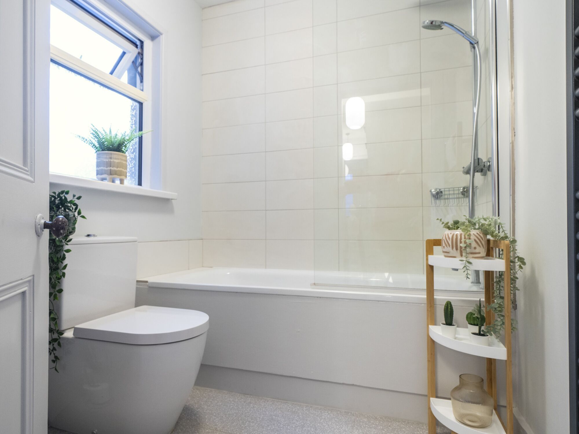 A bathroom with a toilet, a bathtub, and a shower. There is a window with plants on the windowsill.