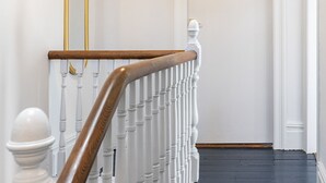 Una escalera con balaustres blancos y una barandilla de madera, que conduce a una puerta con molduras blancas y un pomo dorado.
