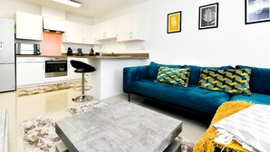 A modern living space with a kitchen, a blue sofa with patterned cushions, and a grey coffee table. - Sleek 1 Bed Apartment w Parking - Pass the Keys (Cardiff)