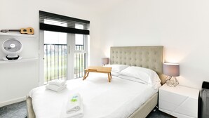 A modern bedroom with a bed, bedside tables, a fan, and a guitar on the wall. - Sleek 1 Bed Apartment w Parking - Pass the Keys (Cardiff)