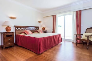 Habitación de hotel con una cama grande, mesitas de noche de madera, una silla y vistas a través de un ventanal.