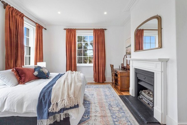 A bedroom with a bed, a dresser, a mirror, and a fireplace. - Devonshire House Luxury with a Fascinating History (North Hobart)