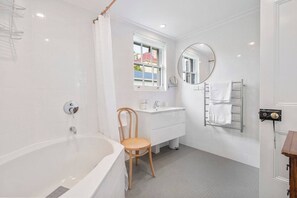 A modern bathroom with a bathtub, a wooden chair, a sink, a mirror, and a towel rack. - Devonshire House Luxury with a Fascinating History (North Hobart)