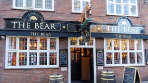 Un pub llamado "The Bear" con una estatua de oso, dos barriles y un cartel de tiza anunciando música en vivo.