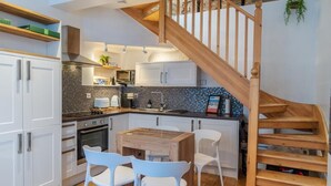 Una cocina moderna con armarios blancos, una escalera de madera y un comedor con sillas blancas.