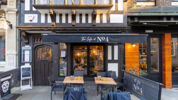 Un café al aire libre con mesas y sillas, un letrero que dice "The Café at No.4", y un toldo negro.
