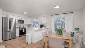 Een moderne keuken met witte kasten, roestvrijstalen apparatuur en een houten eettafel met stoelen.