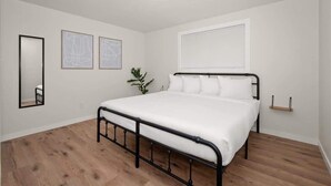Een slaapkamer met een bed, een spiegel en twee afbeeldingen in een lijst aan de muur.
