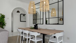 Un coin repas avec une table en bois, des chaises blanches et deux suspensions en osier.