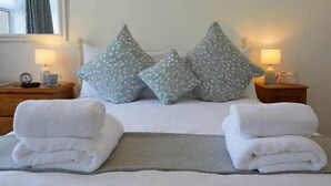 A neatly made bed with two pillows, a bedside table with a lamp, and a window with curtains.