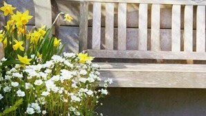 A wooden bench with vertical slats and a stone wall behind it.